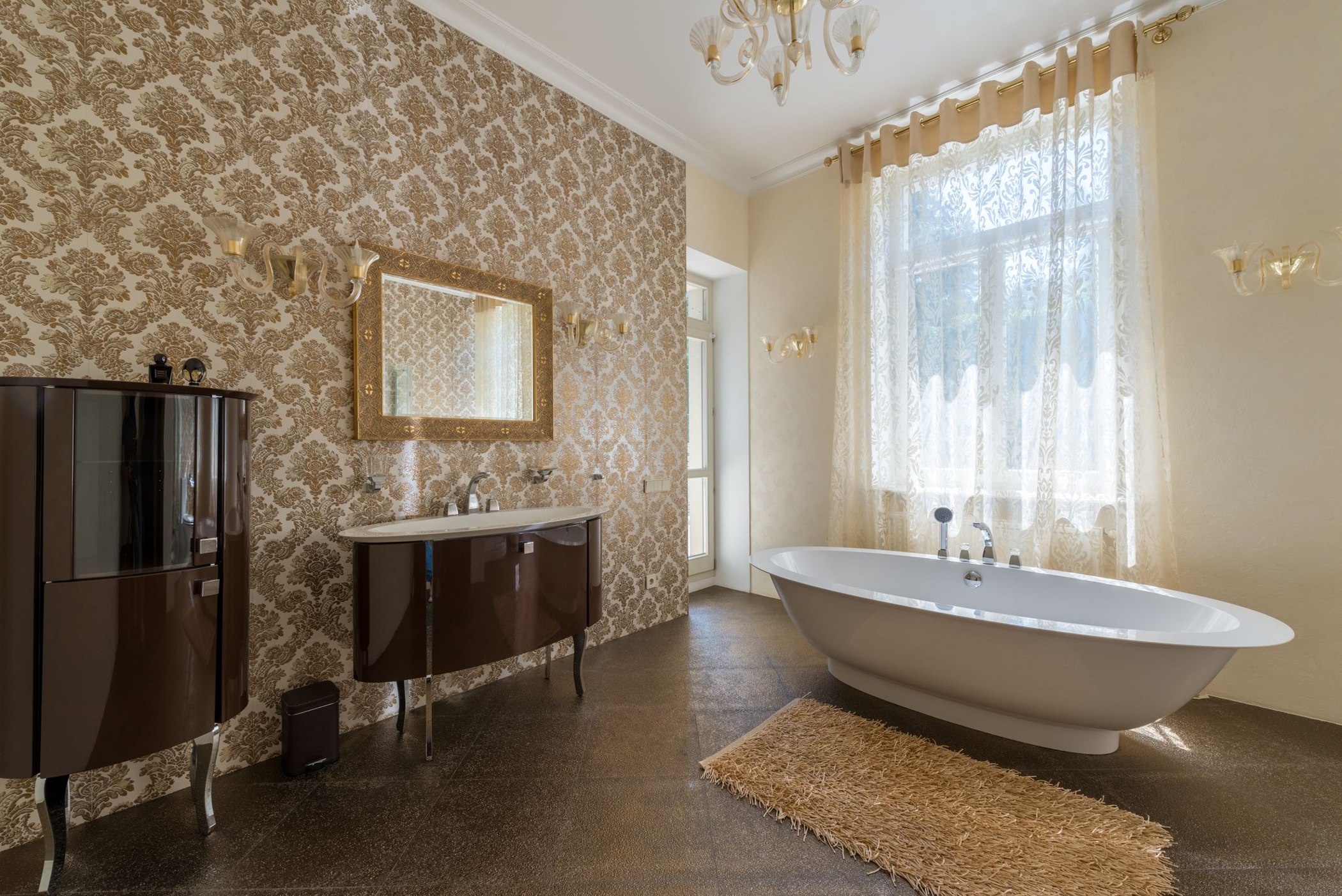 Ornate beige and gold wallpaper covering a bathroom wall beside a freestanding tub