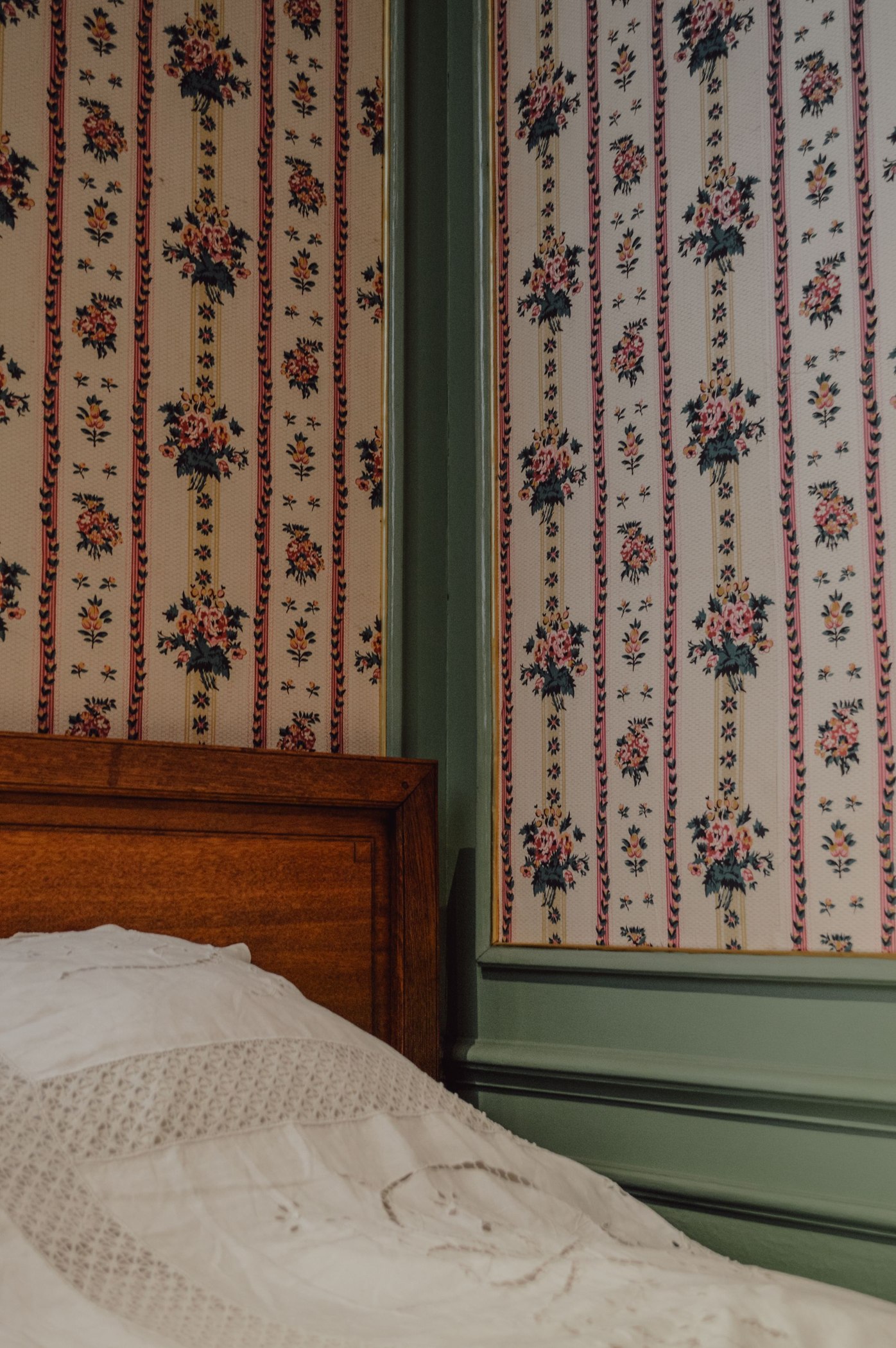 Vintage floral striped wallpaper framed by sage trim above a wooden bed